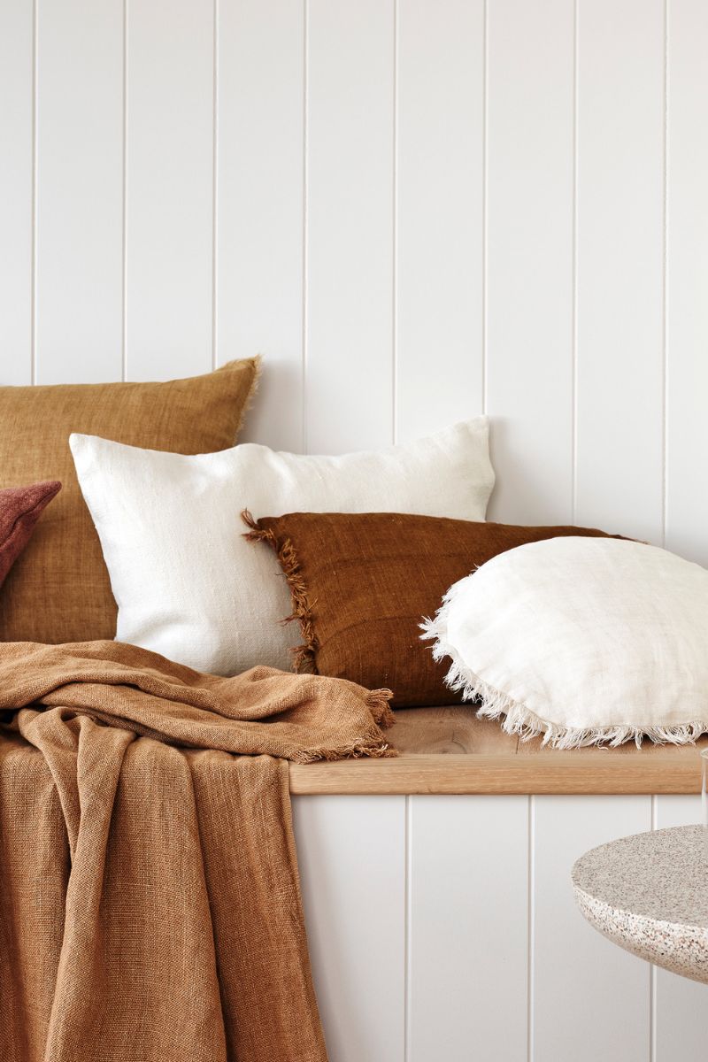 A bunch of cushions all tucked up on a wooden bench with a side table