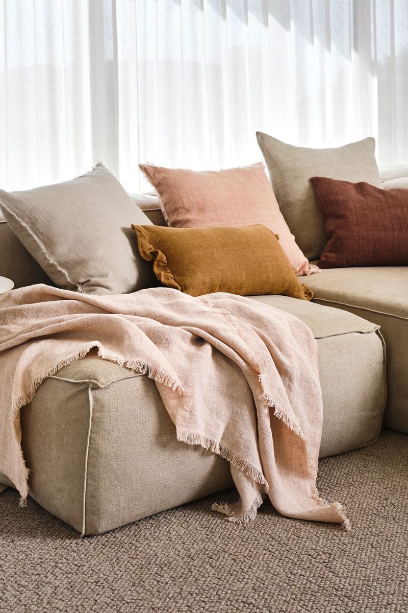 A sofa in a living room with cushions and two throws draped on it.