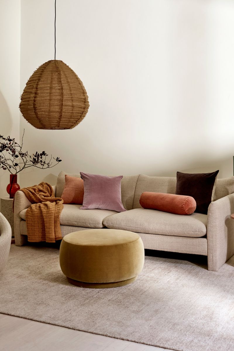 A series of velvet cushions on a couch with a hanging pendant light above
