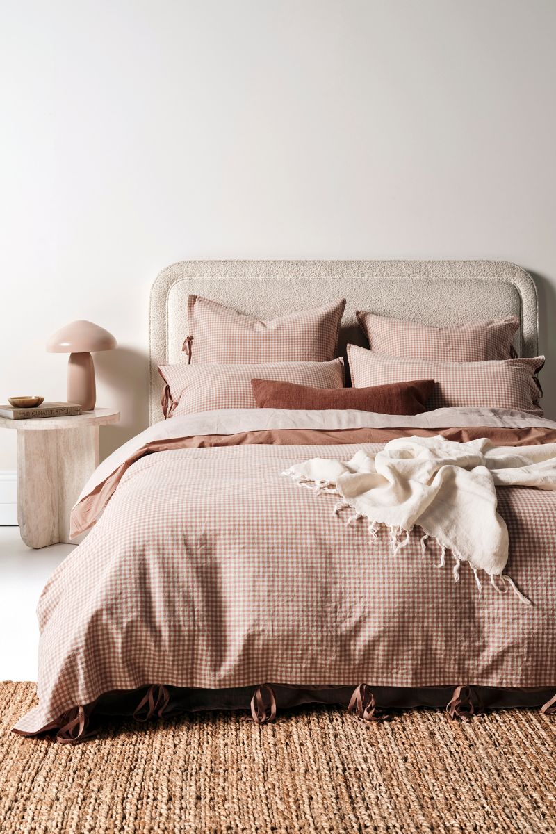 Mini Gingham bedding in Clay on a bed with a throw draped over it – there's a lamp and books next to the bed