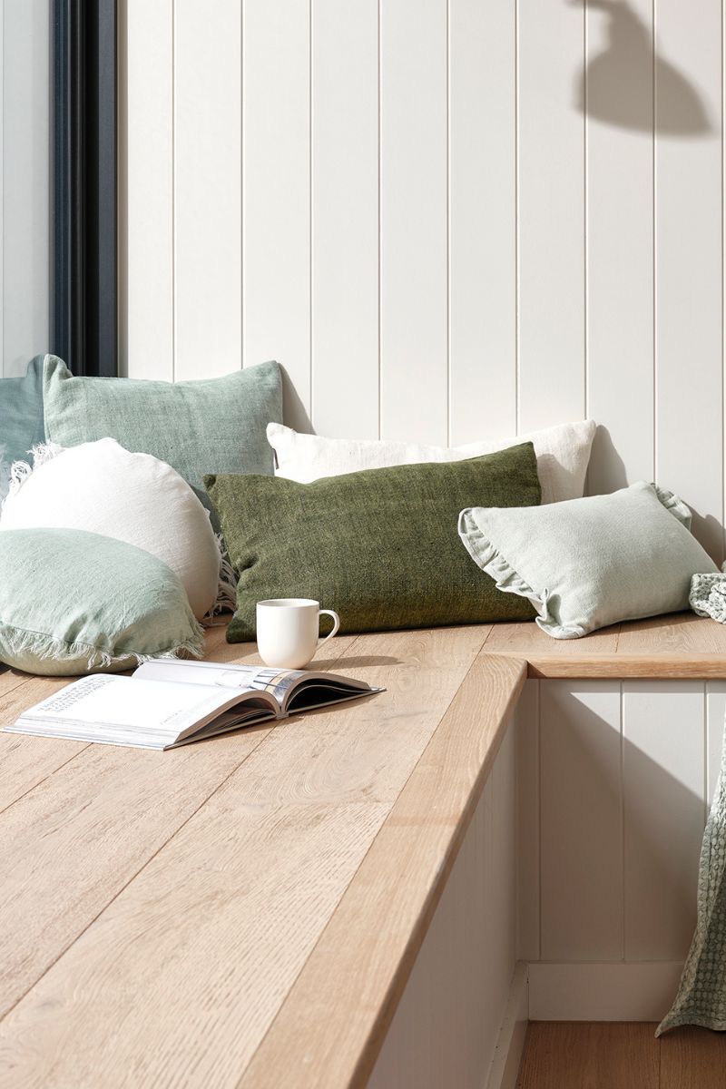 Green cushions with a cup of coffee and a book on a wooden corner bench