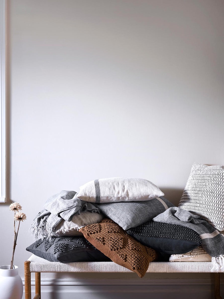 A pile of Husk cushions in Charcoal & Tobacco and Herringbone cushions in Natural and Charcoal