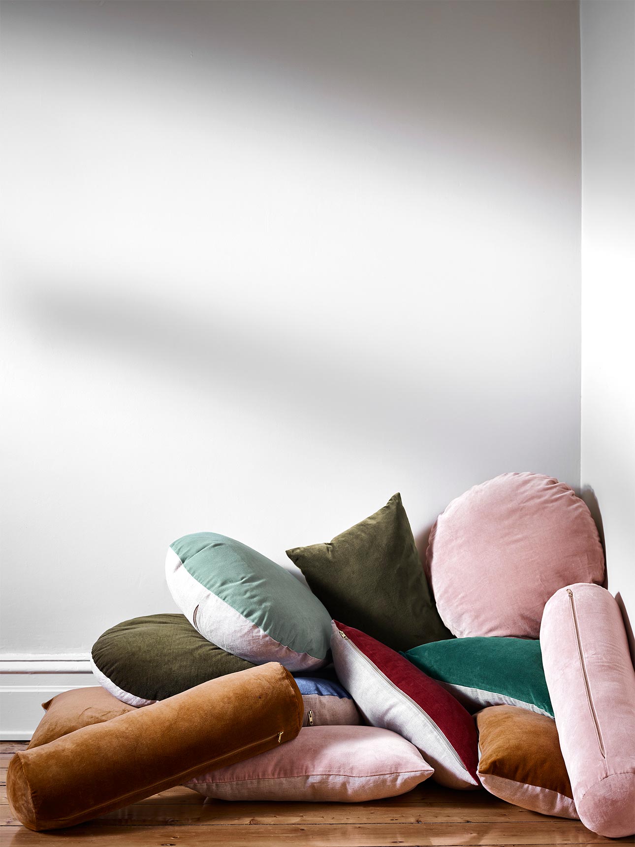 A pile of Luxury Velvet Round Cushions, Bolsters and Square Cushions in Forest Night, Jade, Heather, Caper, Bijou Blue and Hazelnut
